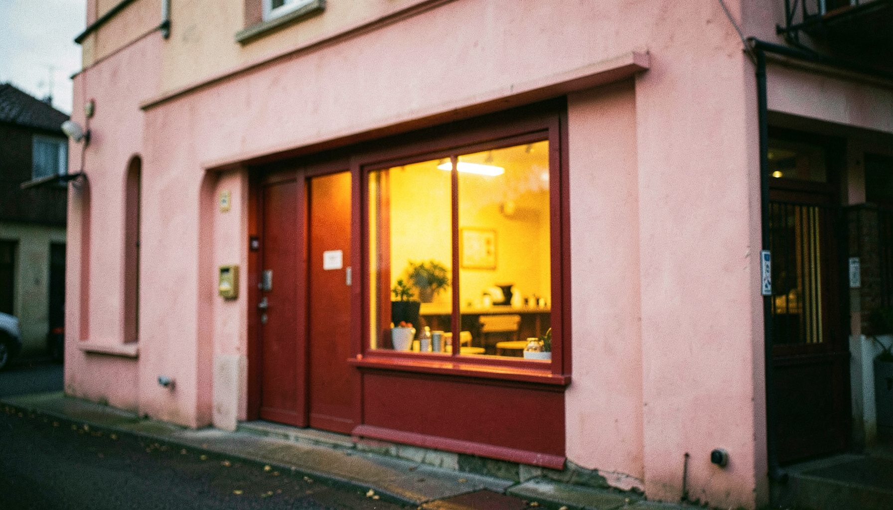 Soft pink and crimson restaurant storefront with a warm glowing window at dusk, shallow depth of field