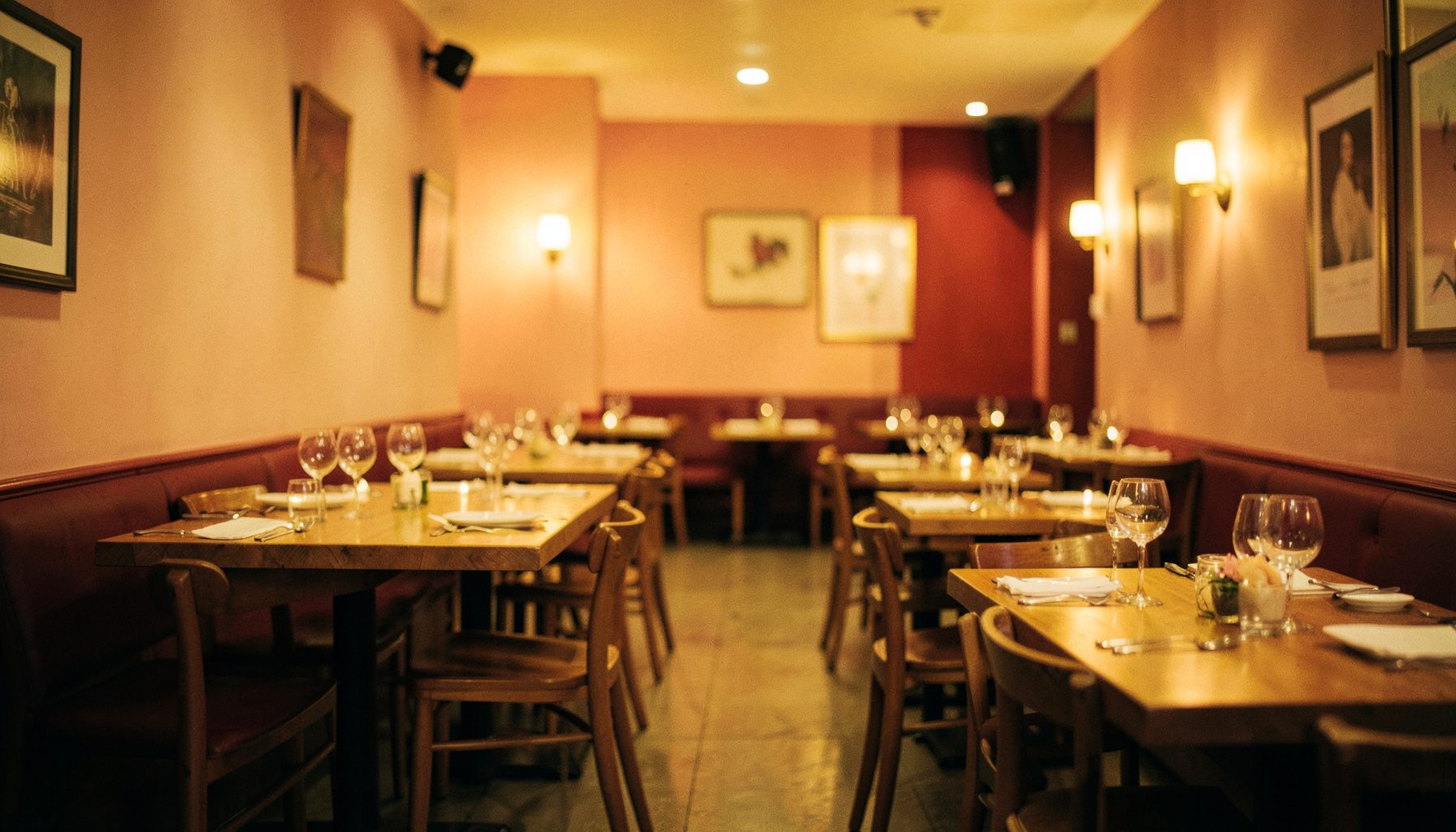 Wide cinematic shot of a warm restaurant interior with soft ambient lighting, blush and crimson wall tones, wooden tables set for service, shallow depth of field.